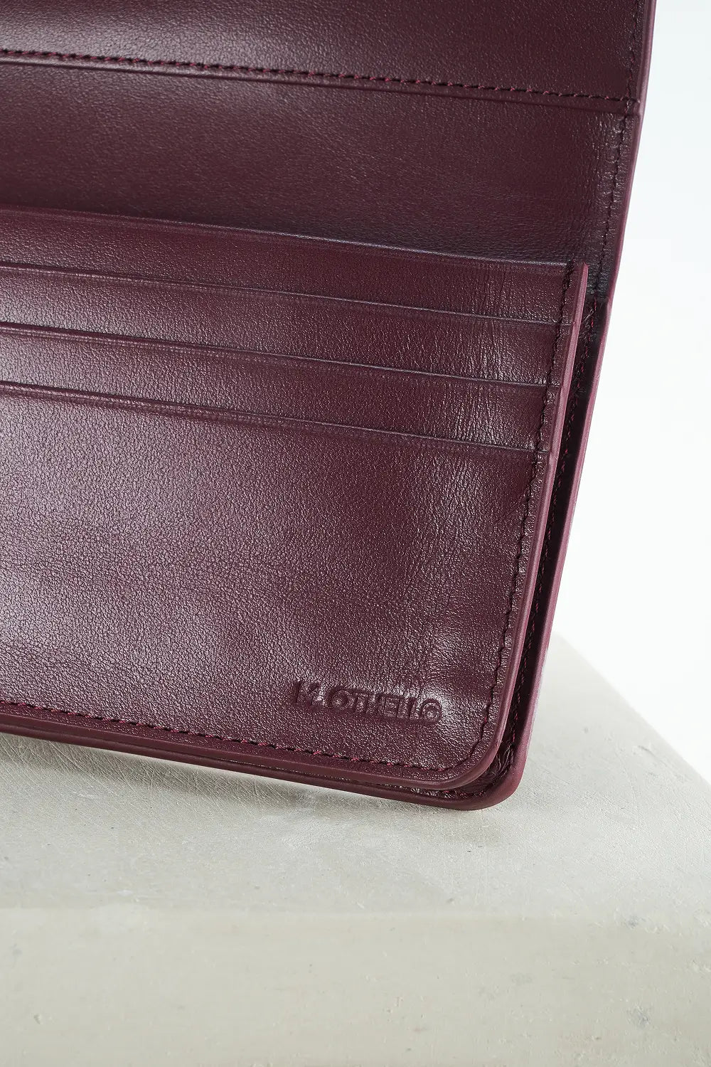 Close-up of a burgundy leather wallet with 'M. Othello' branding on a light gray background.