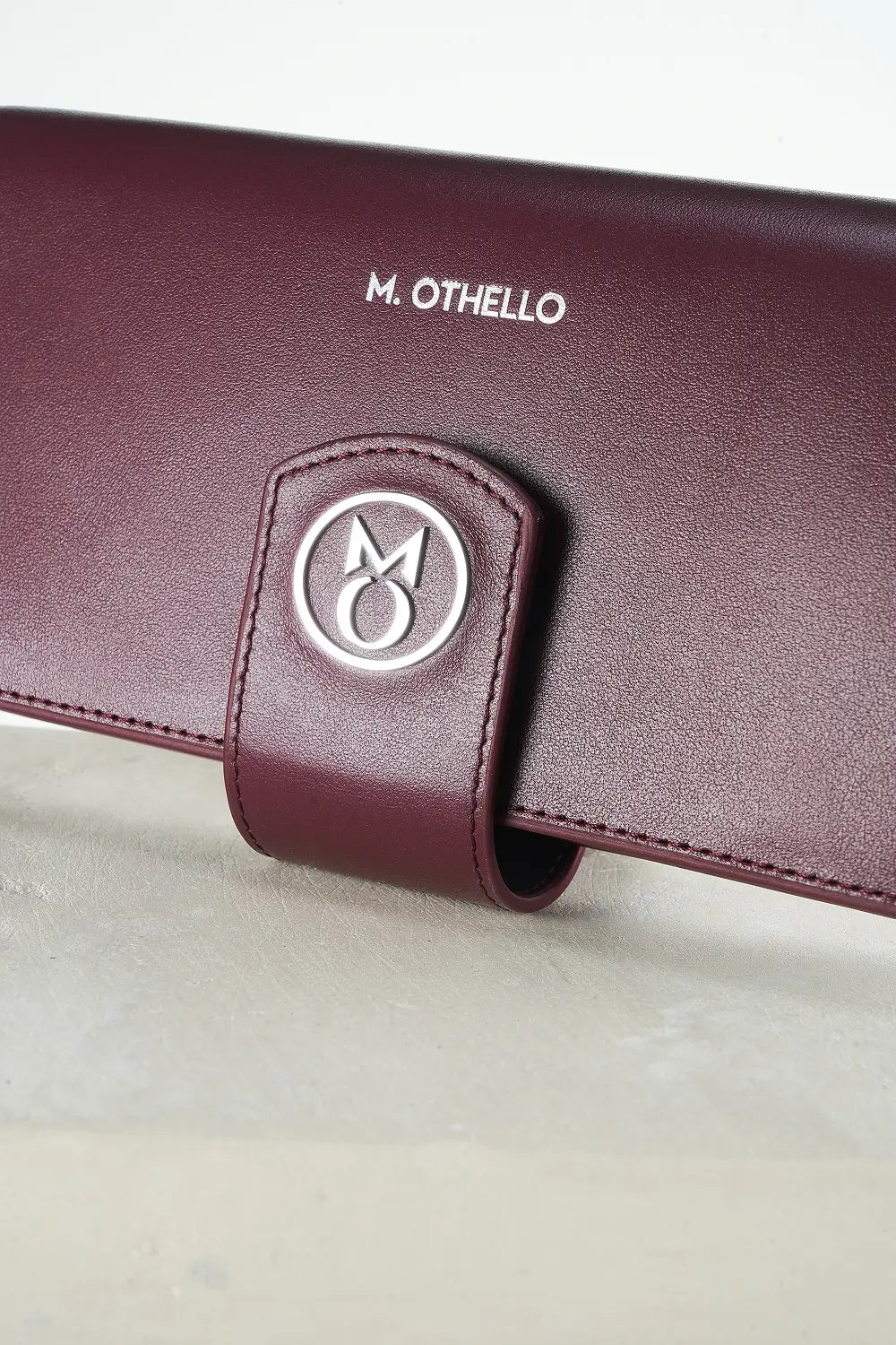 Burgundy leather wallet with 'M. Othello' branding on a light gray background.