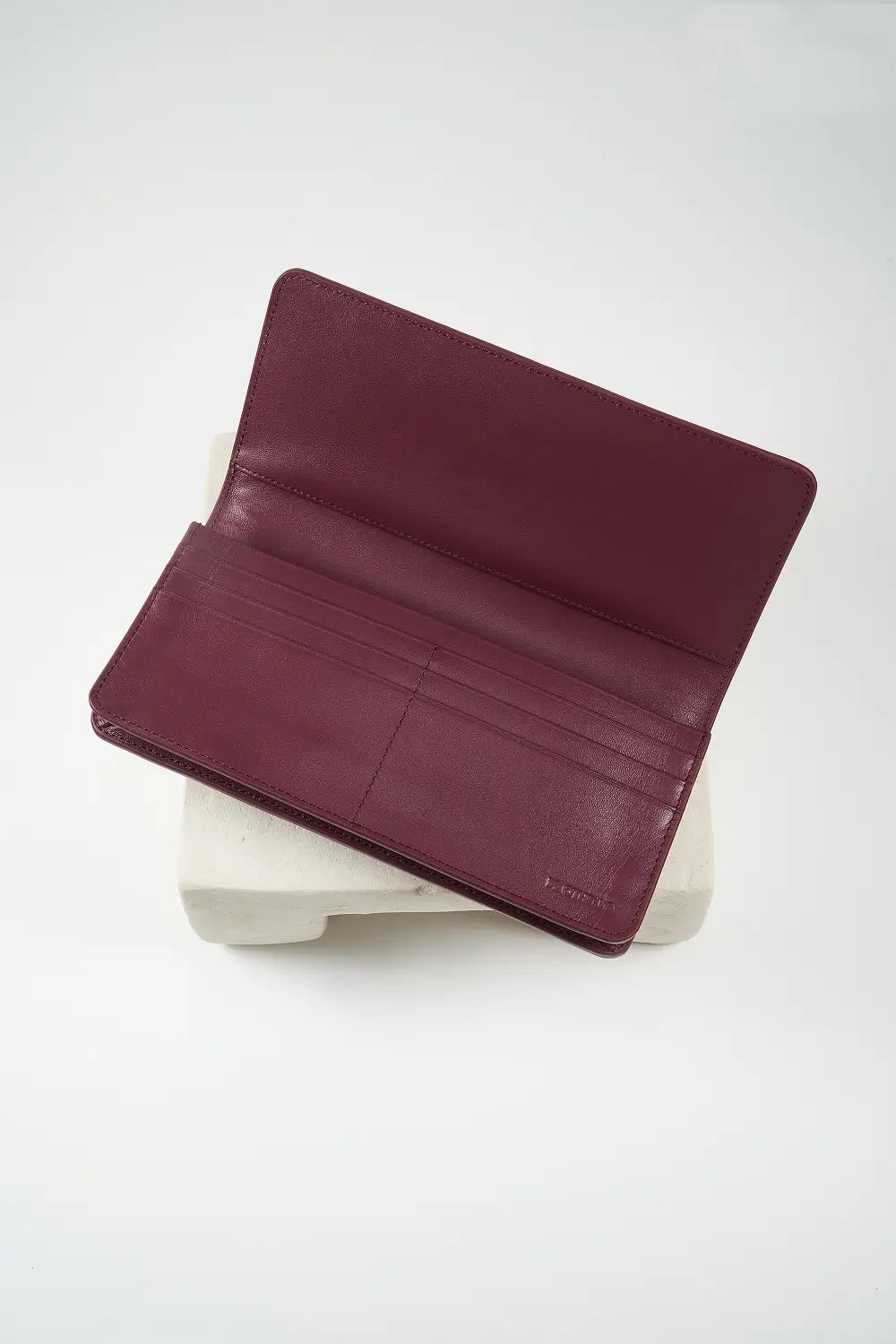 Burgundy leather phone wallet with 'M. Othello' branding on a light gray background.