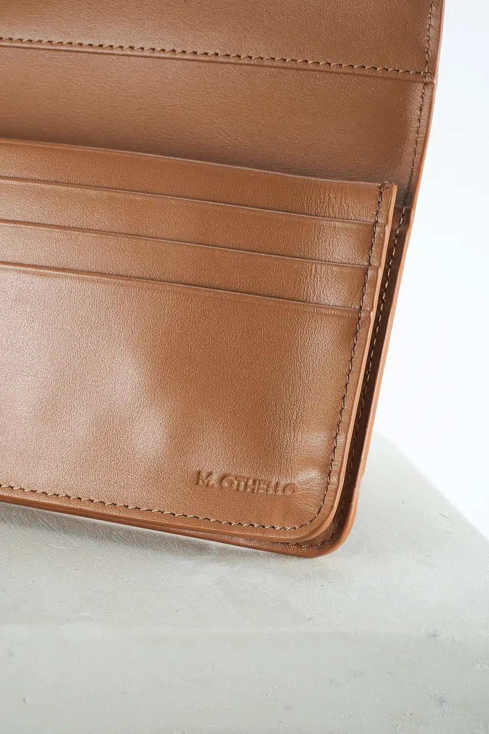 Close-up of a brown leather wallet with visible brand name on a light gray background