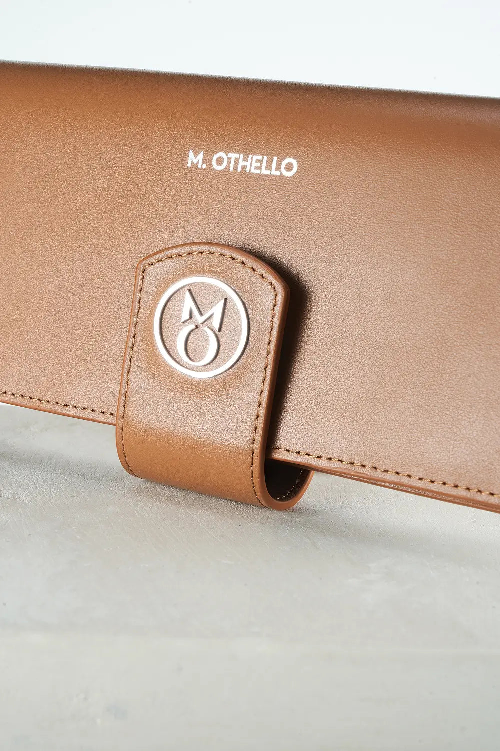 Brown leather product with 'M. Othello' branding on a light gray background