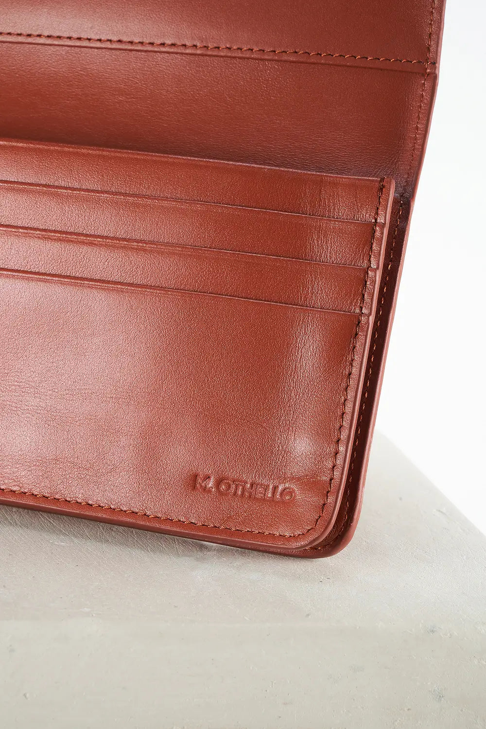 Close-up of a brown leather wallet with 'M.Othello' branding on a light background
