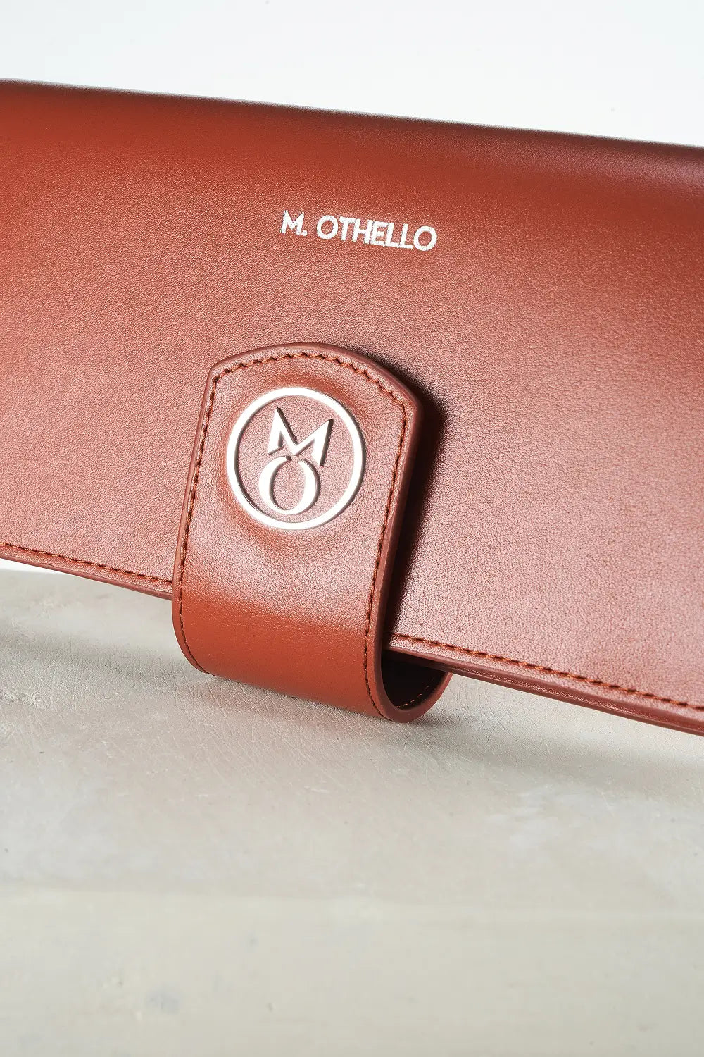 Brown leather wallet with 'M. Othello' branding on a light background