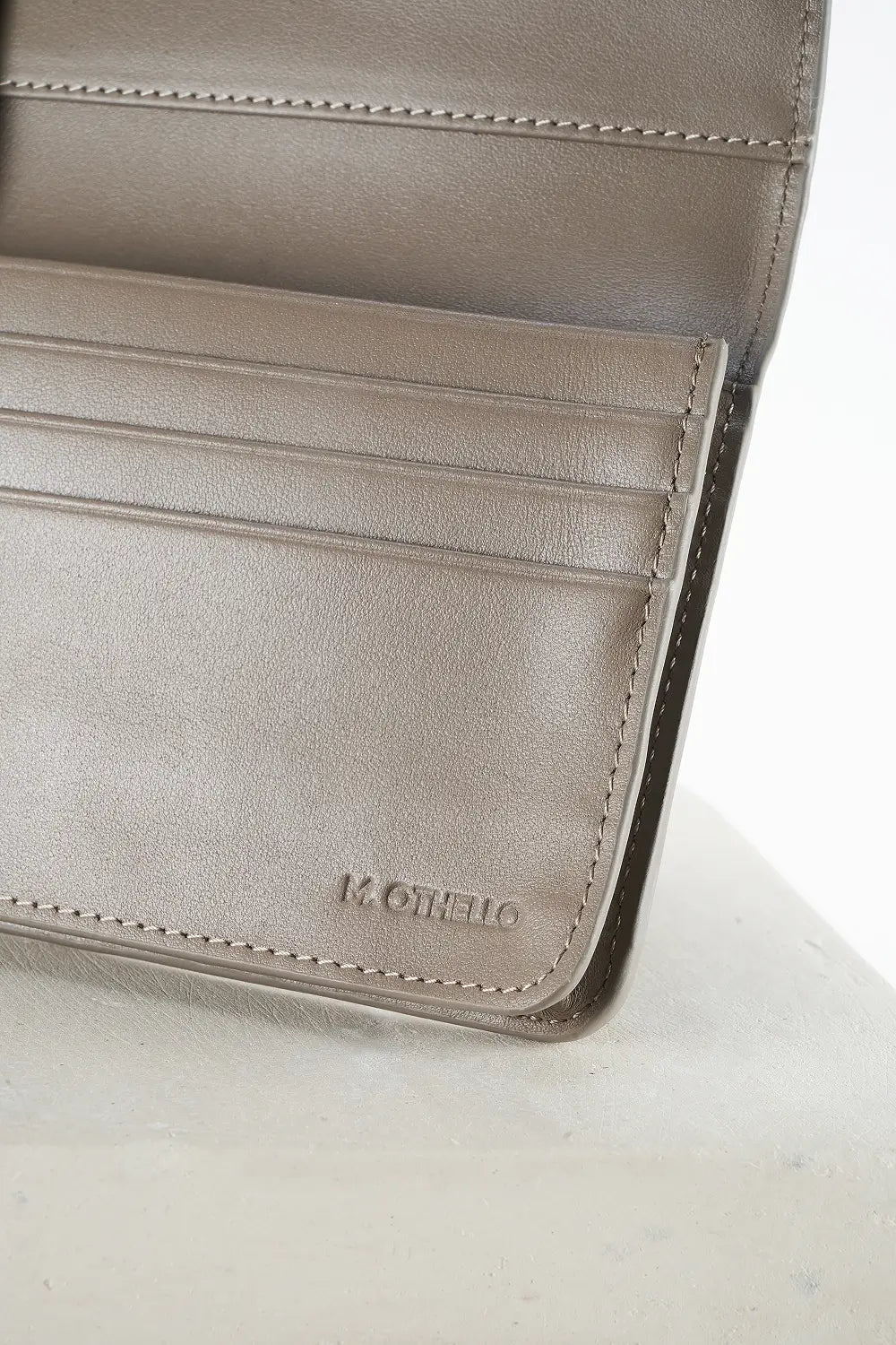 Close-up of a gray leather wallet with 'M. Othello' branding on a light background