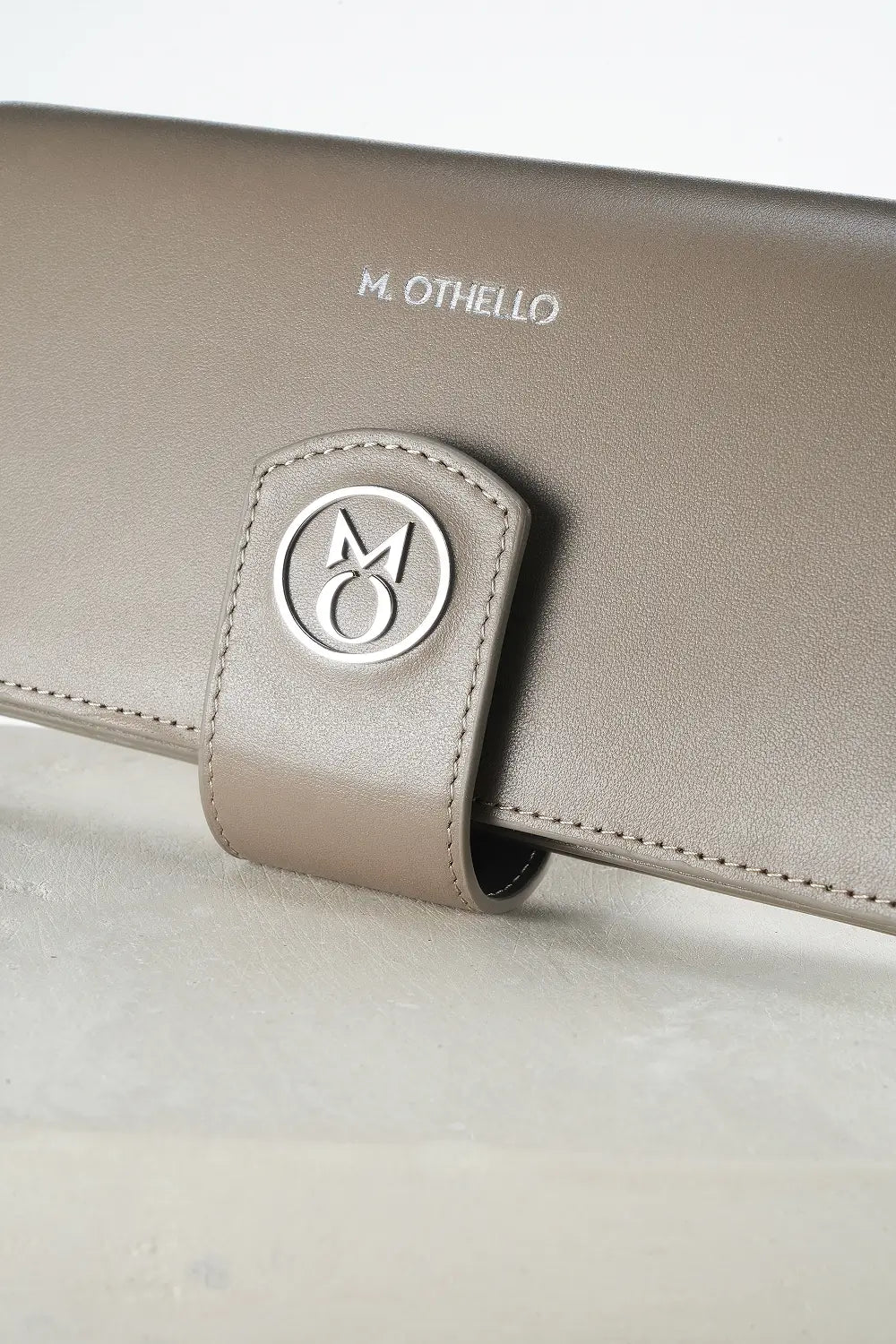 gray leather wallet with 'M. Othello' branding on a light background