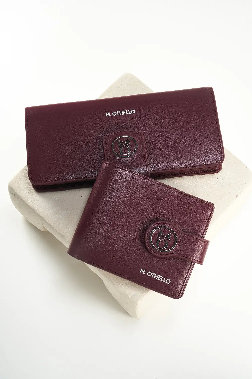 Two burgundy wallets with 'M. Othello' branding on a white surface.